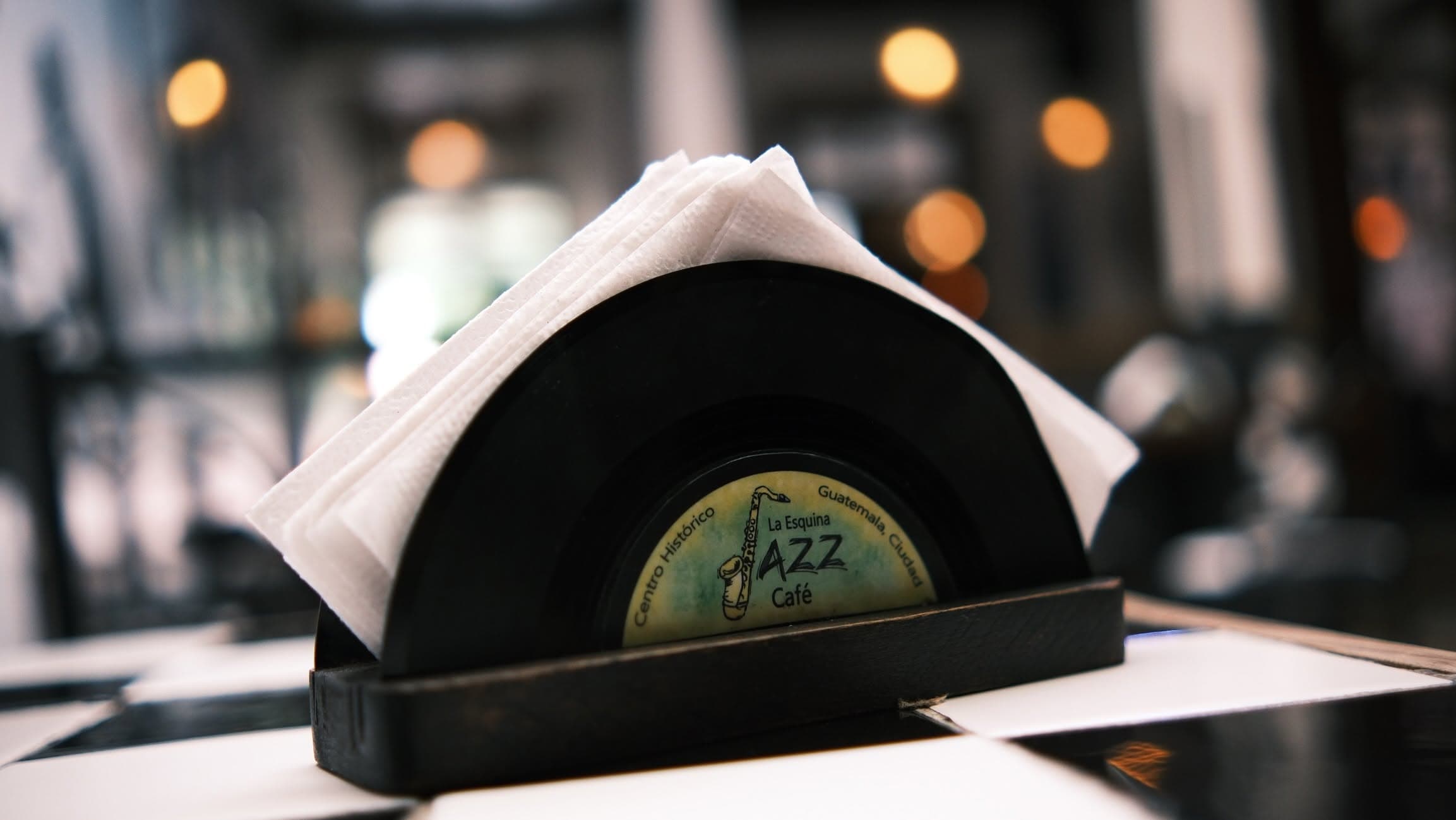 Servilletero hecho con un disco de vinilo, con el logo de La Esquina Jazz Café, sobre el azulejo de ajedrez del salón
